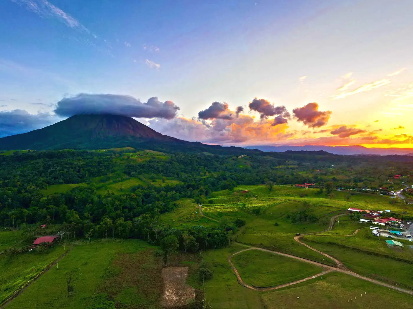 Arenal volcano under a capped cloud at sunset above green pastures near La Fortuna, Costa Rica