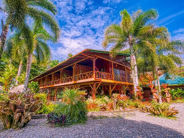 The wooden main house of Hotel Banana Azul with its balcony, framed by palms