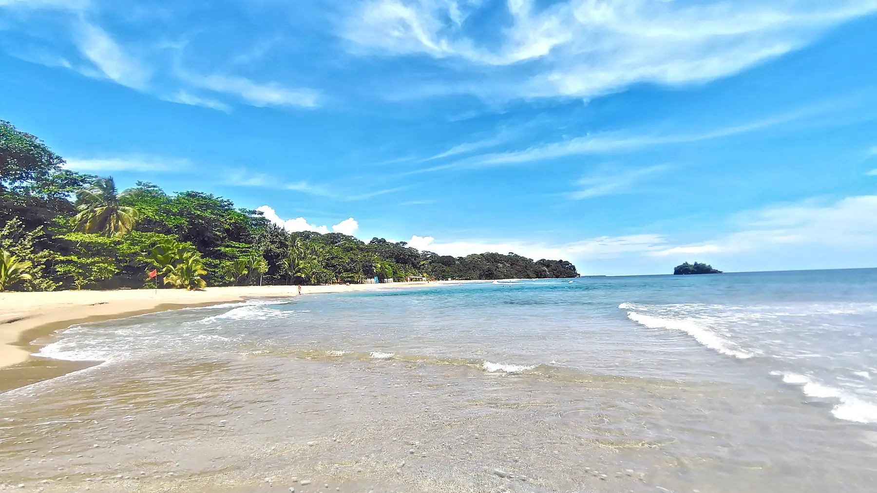 A long beach with a small rocky island offshore at Playa Cocles