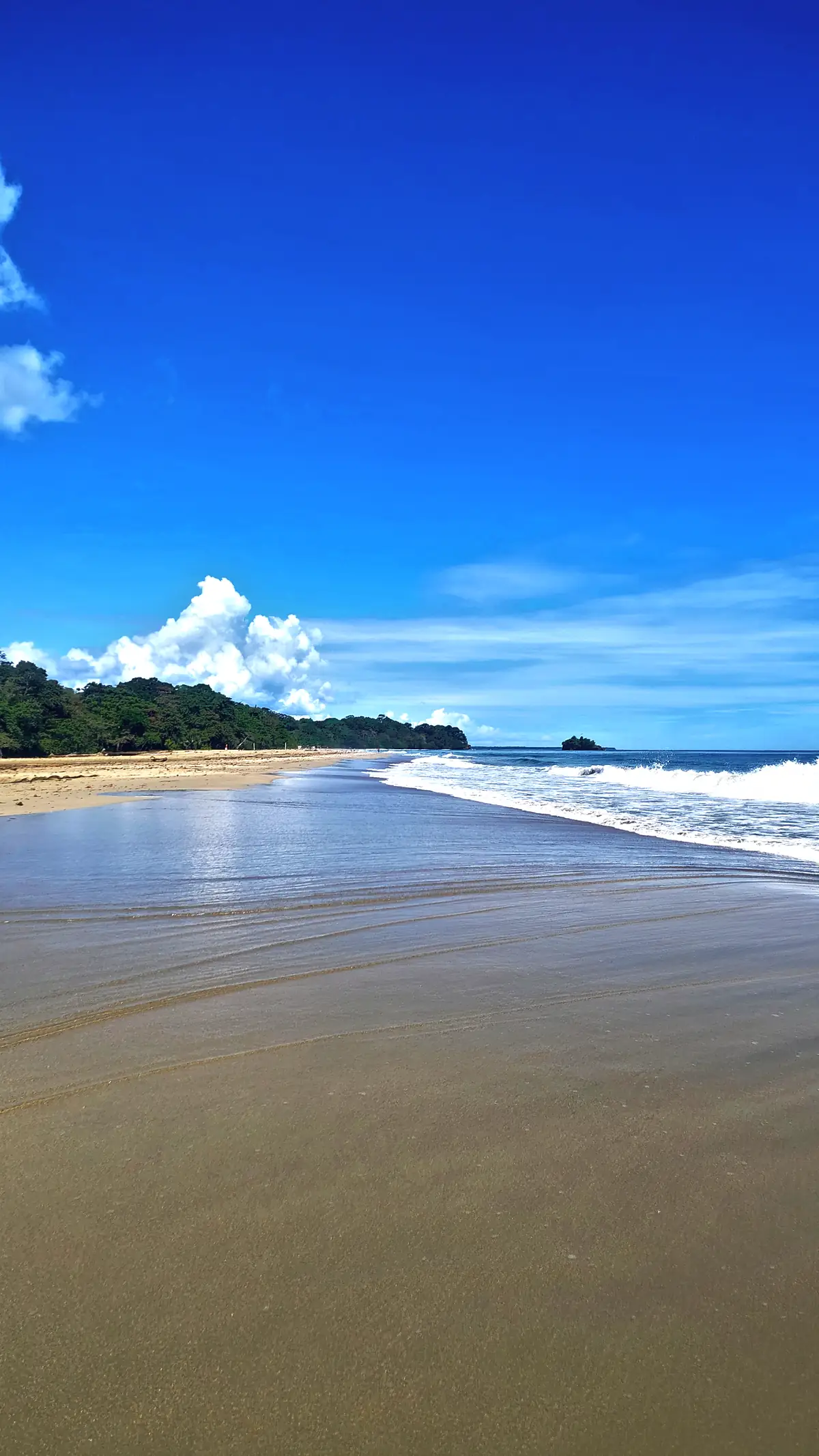 Wet sand and a deep blue sky at Playa Cocles