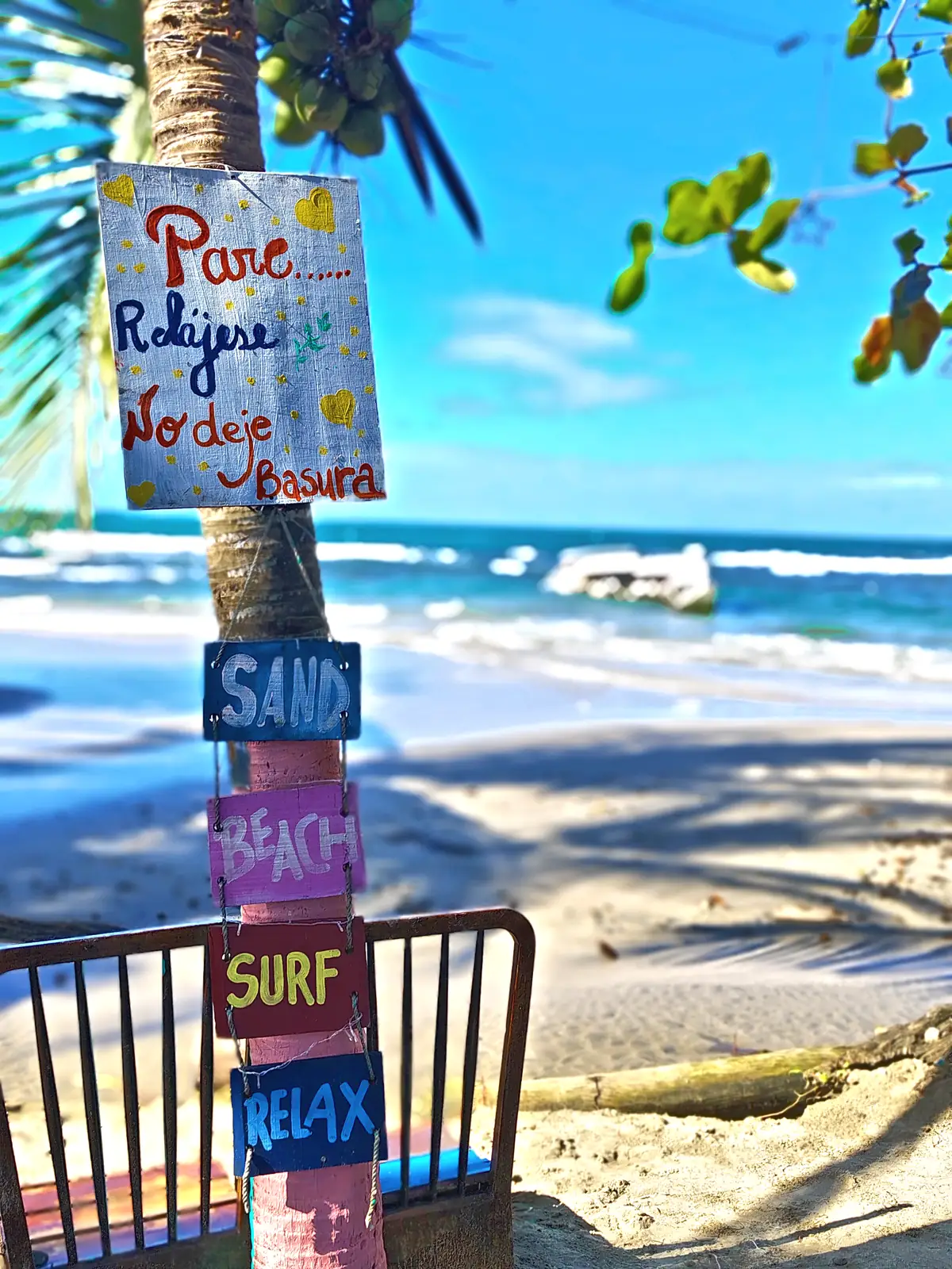 A hand-painted signpost on a beach tree reading sand, surf and relax